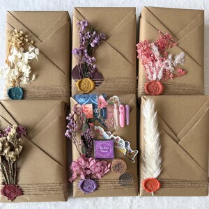 May include: Six rectangular packages wrapped in brown paper, each adorned with dried flowers, twine, and wax seals in various colors. Some packages feature stickers and decorative elements. The overall aesthetic is rustic and artisanal.