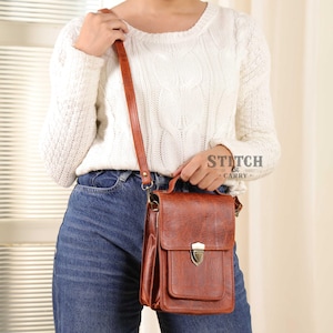 May include: A brown leather crossbody bag with a flap closure and a top handle. The bag has a textured surface and a long, adjustable strap. The text "STITCH & CARRY" is visible on the right side of the image.