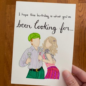 May include: A birthday card with a hand-drawn illustration of two people holding microphones. The card reads, "I hope this birthday is what you've been looking for..." The illustration features a person in a green hat and another in a pink top.
