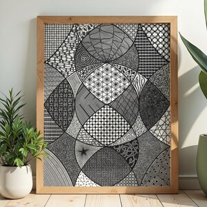 May include: A framed black and white abstract art print. The artwork features a geometric design with various patterns and textures. The frame is made of light-colored wood. The print is displayed on a wooden floor, with potted plants on either side.