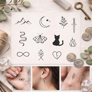 May include: A collection of temporary tattoo designs featuring various black line art illustrations. Designs include mountains, a crescent moon, a sprig, a dagger, a snake, a butterfly, a cat, flames, an infinity symbol, a stylized flame, and a broken heart.