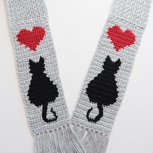 Echarpe chat au crochet. Téléchargez le fichier pdf pour réaliser cette écharpe grise avec des silhouettes de chats noirs et des coeurs rouges. Cadeaux pour les amoureux des chats
