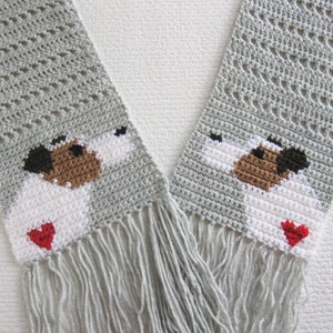 May include: Gray crocheted scarf with two white dog faces and red hearts. The scarf has fringe on the ends.