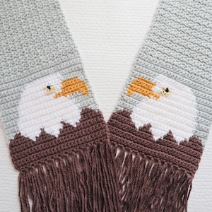 May include: A crocheted scarf with a brown fringe and two white bald eagle heads with yellow beaks. The eagle heads are crocheted on a brown background.