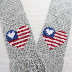 May include: A gray crocheted scarf with two American flag hearts. The hearts are red, white, and blue with a white heart in the center of each.