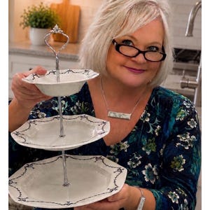 May include: A three-tiered serving tray with white porcelain plates and a silver metal handle. Each plate has a scalloped edge with a dark blue floral design. The tray is ideal for serving desserts or appetizers.