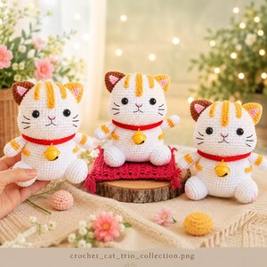Könnte beinhalten: Drei gehäkelte Katzenfiguren in Weiß und Orange, die jeweils ein rotes Halsband mit einer kleinen gelben Glocke tragen. Die Katzen haben schwarze Augen, rosa gestickte Nasen und gestreifte Ohren. Die mittlere Katze sitzt auf einer roten Matte.