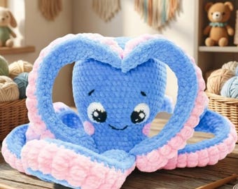 Può includere: Un peluche a forma di polpo all'uncinetto con testa e corpo blu brillante e accenti rosa tenue sui tentacoli. Il polpo ha grandi occhi ricamati e un piccolo sorriso. È appoggiato su una superficie di legno con due uncinetti e un metro a nastro.