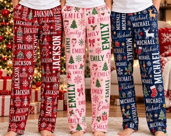 Può includere: Tre paia di pantaloni da pigiama con motivi natalizi festivi. Il paio a sinistra è a quadri rossi con il nome Jackson, quello centrale è rosa chiaro con il nome Emily e quello a destra è a quadri blu navy con il nome Michael.