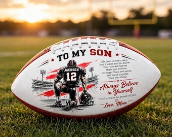 Può includere: Un pallone da football bianco e marrone con la grafica di un giocatore in ginocchio su un campo, il testo TO MY SON, un messaggio motivazionale e la firma Love, Mom. Il pallone ha lacci bianchi e una striscia rossa.