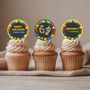 May include: Three cupcakes with white frosting, each topped with a circular decoration. The decorations feature colorful block designs and birthday messages: "Happy Birthday Jonathan", "I was 67, now I'm 7", and "Jonathan's 7th Birthday".