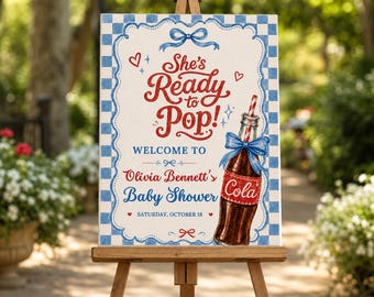 Puede incluir: Un letrero rectangular con borde de cuadros azules y blancos que presenta el texto rojo She's Ready to Pop! y una botella de refresco de vidrio marrón con un lazo azul y una pajita a rayas rojas y blancas. El texto dice Welcome to Olivia Bennett's Baby Shower.