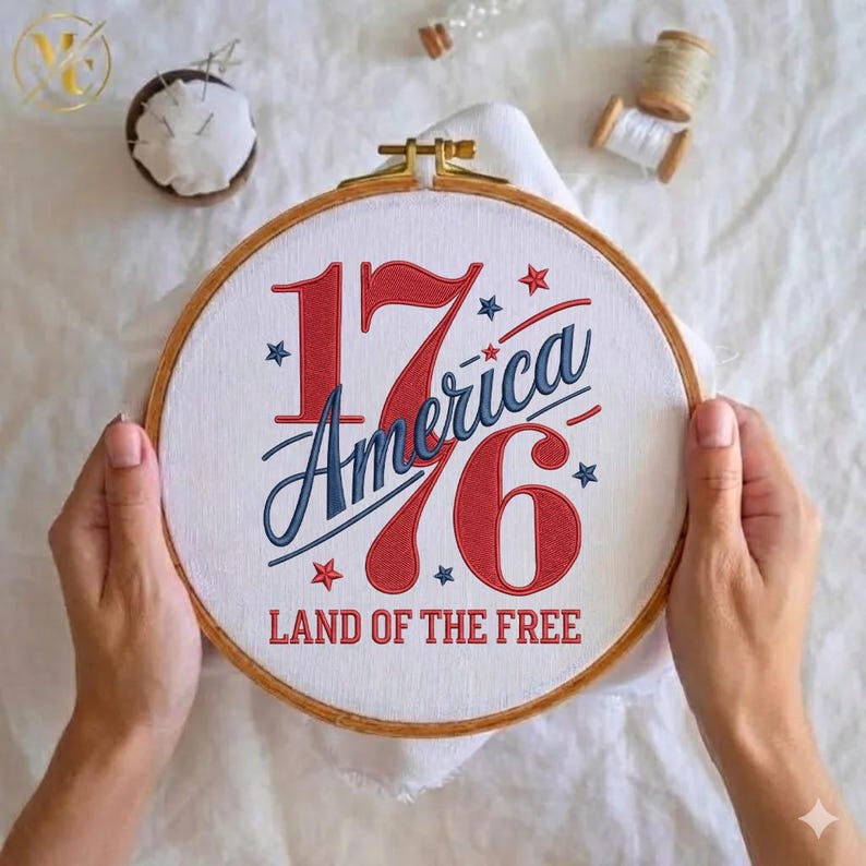 K&ouml;nnte beinhalten: Ein runder Stickrahmen mit dem Text "1776 America Land of the Free" in Rot und Blau. Die Stickerei befindet sich auf wei&szlig;em Stoff und wird von H&auml;nden gehalten. Im Hintergrund befinden sich N&auml;hutensilien.