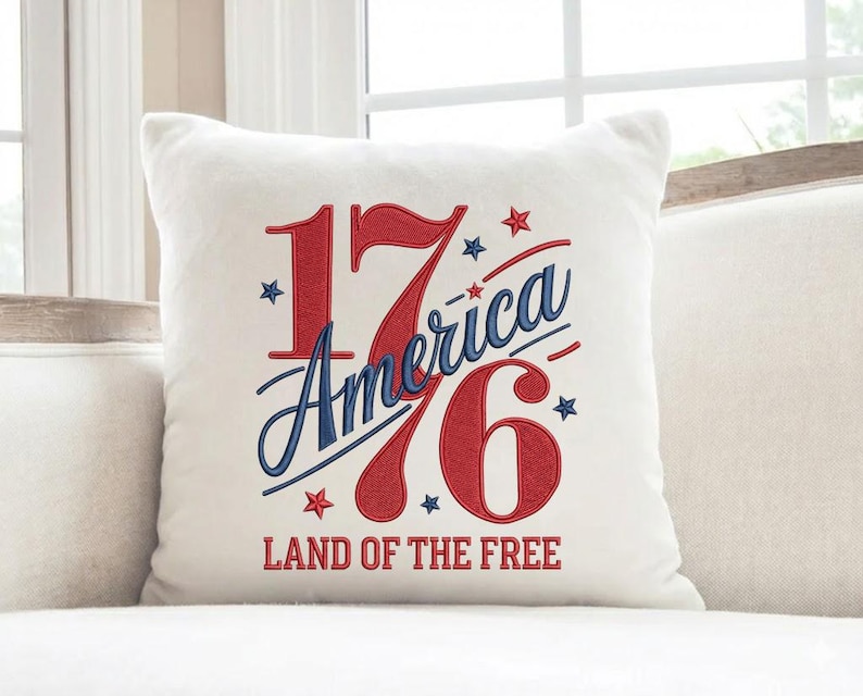 K&ouml;nnte beinhalten: Ein quadratisches wei&szlig;es Kissen mit dem Text "1776 America Land of the Free" in Rot und Blau. Die Zahlen und der Text sind gestickt, mit Sternakzenten.