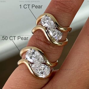 May include: Two gold rings with pear-cut diamonds are shown. One ring is labelled "1 CT Pear" and the other "1.50 CT Pear". The rings have a distinctive, flowing design, highlighting the sparkling diamonds.