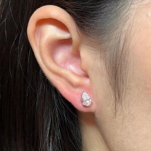May include: A single pear-shaped stud earring featuring a clear, faceted gemstone set in a polished silver-toned metal base. The earring is positioned securely in the earlobe, showcasing a brilliant, reflective surface and a classic teardrop silhouette.