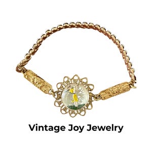 May include: Vintage gold-toned bracelet with a central round charm featuring a miniature scene. The charm is surrounded by a decorative, openwork frame. The bracelet has a delicate chain and ornate details. The text "Vintage Joy Jewelry" is at the bottom.