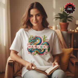 May include: White t-shirt featuring a colorful dragon design with the word "MAHJONG" in block letters. The dragon is teal, yellow, and blue, surrounded by pink flowers and bamboo. The shirt is a casual wear item.