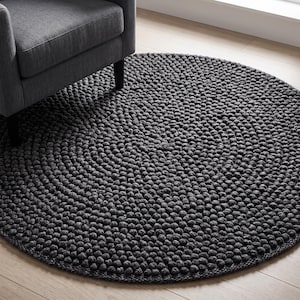 May include: A round, dark grey area rug featuring a dense, textured surface composed of numerous small, spherical, felted wool-like knots arranged in a concentric circular pattern, providing a uniform and tactile appearance across the entire rug.