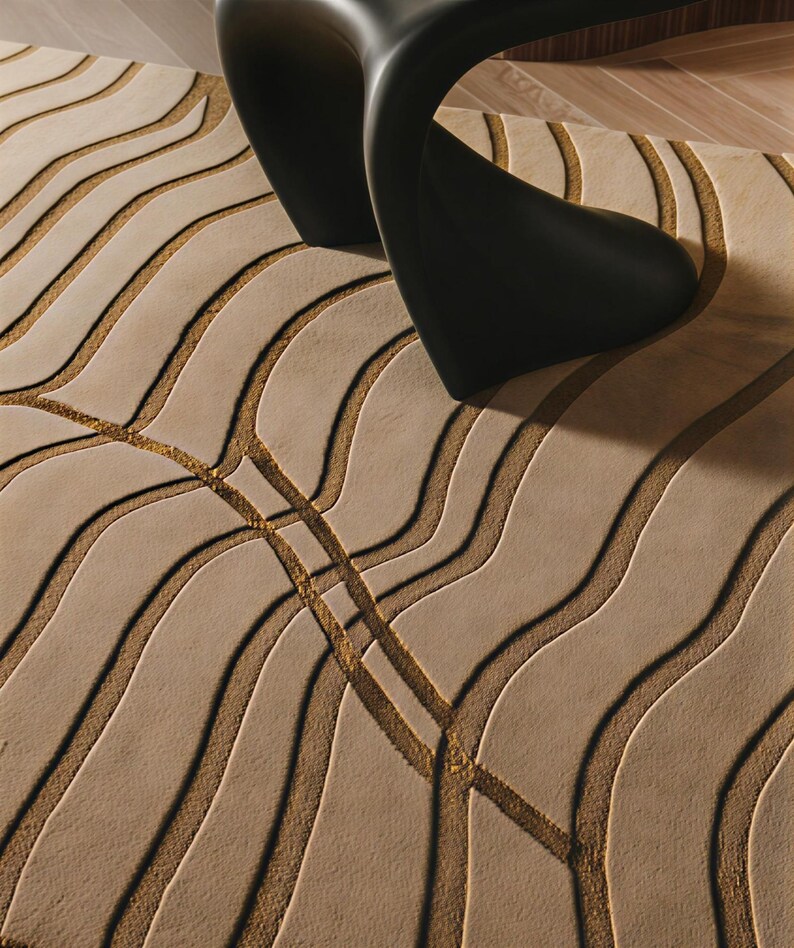 May include: A beige area rug featuring a textured pattern of raised, undulating wave lines in a darker tan shade, with a smooth black curved furniture piece resting on the surface of the rug, partially obscuring the view of the floor covering.