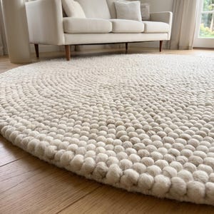 May include: A large, circular area rug crafted from numerous small, off-white felted wool balls arranged in a dense, concentric pattern. The rug features a thick, textured surface composed of individual spherical wool elements.