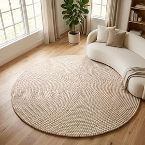 May include: A large, circular area rug featuring a dense, textured surface composed of numerous small, uniform, cream-colored felted wool balls arranged in a concentric, spiraling pattern that radiates outward from the center.
