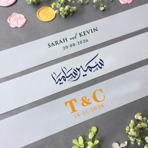 May include: Three white ribbons with text for a wedding. The top ribbon reads "SARAH and KEVIN" and "20.08.2026" in green. The middle ribbon has Arabic script in navy blue. The bottom ribbon reads "T & C" and "16.11.2026" in orange.