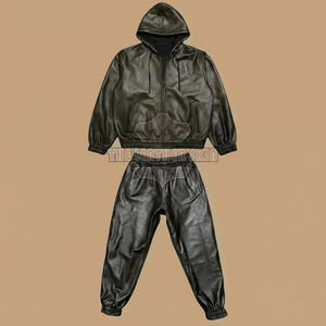 May include: A black leather two-piece outfit, comprising a hooded zip-up jacket and matching sweatpants. The jacket features a front pocket and ribbed cuffs and hem. The sweatpants have an elasticated waistband and cuffs. The text "THE LEATHER SKIN" is visible.