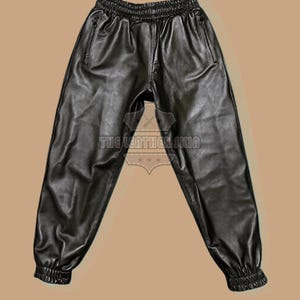 May include: Black leather joggers with an elasticated waistband and cuffs. The trousers have two front pockets with zips. The text "THE LEATHER SKIN" is visible on the garment.