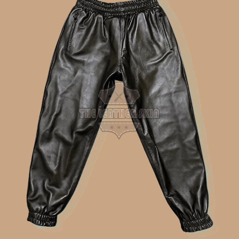 May include: Black leather joggers with an elasticated waistband and cuffs. The trousers have two front pockets with zips. The text "THE LEATHER SKIN" is visible on the garment.
