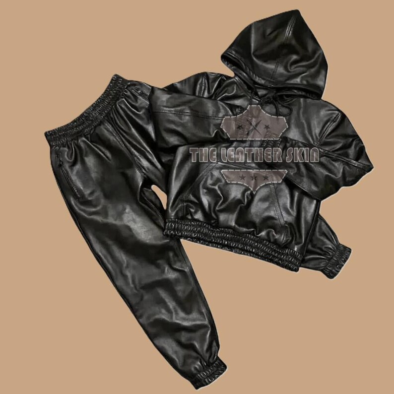 May include: Black leather hoodie and matching trousers set. The hoodie features a drawstring hood, elasticated waist and cuffs. The trousers have an elasticated waistband and cuffs. The text "THE LEATHER SKIN" is visible on the hoodie.