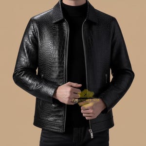 Könnte beinhalten: Schwarze Lederjacke mit Krokodilhautstruktur. Die Jacke hat einen Reißverschluss, einen Kragen und zwei Seitentaschen. Die Ärmel sind lang und die Jacke wird über einem schwarzen Rollkragenpullover getragen.