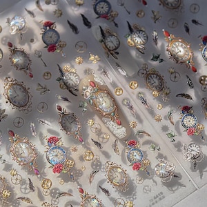 Puede incluir: Hojas transparentes de pegatinas para uñas con diseños de relojes ornamentados en oro, plata y azul, acentuados con rosas rojas, engranajes y plumas. Estética vintage y steampunk.