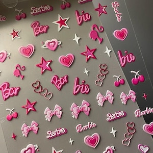 Peut inclure: Feuille d'autocollants roses et blancs avec divers motifs, notamment des cœurs, des étoiles, des nœuds, des cerises, des flamants roses et le mot "Barbie". Les autocollants sont dans des tons de rose et de blanc.