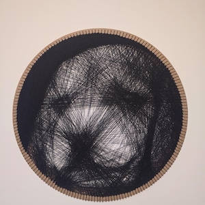 Pode incluir: Uma peça de arte em fio redonda com um design de fio preto em uma moldura de madeira marrom clara. O fio preto é densamente tecido, criando um padrão abstrato texturizado. A obra de arte é montada em um fundo branco.