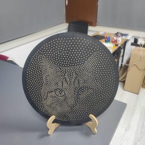 May include: A black decorative plate with a pattern of small, evenly spaced white dots. The plate is displayed on a light-colored wooden stand, set against a neutral background.