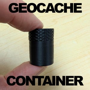 May include: Black geocache container with a textured top. The word "GEOCACHE" is printed above the container, and the word "CONTAINER" is printed below it. The container is held between two fingers.