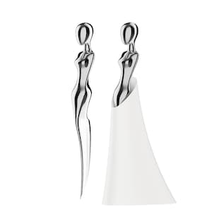 Può includere: Due tappi per bottiglia argentati a forma di figura astratta. Un tappo è da solo, mentre l'altro è inserito in un supporto bianco a forma di cono. I tappi hanno un design elegante e moderno.