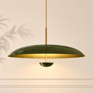 Op de afbeelding: Een hanglamp met een brede, schotelvormige kap in een glanzende olijfgroene afwerking. De binnenkant van de kap is goudkleurig en hangt aan een dunne messing stang. Een kleine, bijpassende olijfgroene koepel bevindt zich in het midden onderaan.