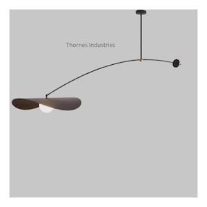 Op de afbeelding: Moderne zwarte hanglamp met een gebogen arm en een grote, bloemblad-vormige kap. De lamp heeft een klein, rond contragewicht en een centrale lichtbron. De tekst "Thornes Industries" is zichtbaar.