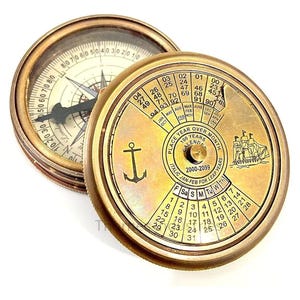 May include: A vintage brass compass and calendar. The compass features a rotating dial with directional markings. The calendar displays a 100-year calendar from 2000-2099, with an anchor symbol and a ship illustration.