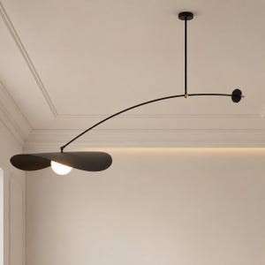 May include: A black pendant light fitting featuring a long, curved metal arm suspended from the ceiling. The fitting includes a single white spherical glass bulb nestled beneath a wide, flat, black disc-shaped shade, with a small gold accent.