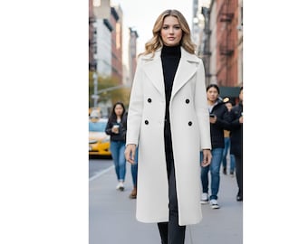 May include: A long, white double-breasted coat with black buttons. The coat is worn over a black turtleneck and black pants. The image is taken on a city street with people walking in the background.