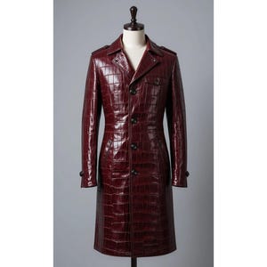 May include: A burgundy, long leather trench coat with a crocodile texture. The coat features a notched collar, button closures, and epaulettes. The coat is displayed on a mannequin.