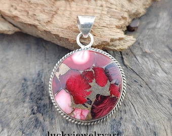 May include: A circular pendant with a silver loop and a patterned stone. The stone has red, pink, and gold hues, framed by a silver rope design. The text "luckyjewelryart" is visible at the bottom of the image.