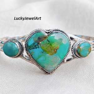 May include: A silver cuff bracelet featuring a large heart-shaped turquoise stone in the centre and two smaller round turquoise stones on the sides. Each stone is set in a twisted silver wire border. The text LuckyJewelArt is visible above.
