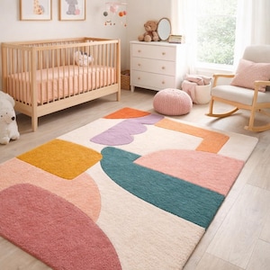 May include: A colourful, abstract rug in a nursery setting. The rug features geometric shapes in shades of pink, orange, yellow, teal, and purple. A wooden cot, chest of drawers, and rocking chair complete the room's decor.