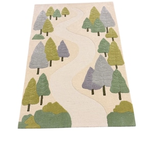 Puede incluir: Una alfombra rectangular con un diseño de bosque caprichoso. La alfombra presenta un fondo color crema con un camino sinuoso y varios árboles en tonos de verde, gris y amarillo. Los árboles están dispuestos a lo largo del camino, creando una estética lúdica inspirada en la naturaleza.