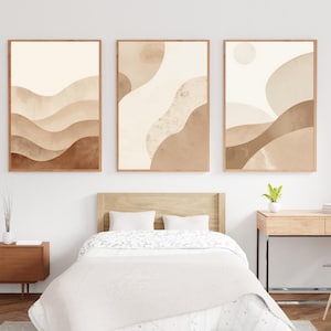 May include: Three framed abstract art prints with a neutral color palette of beige, brown, and cream. The artwork features watercolor-style designs of layered shapes and organic forms, creating a calming aesthetic. The frames are a warm wood tone.