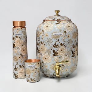 May include: A set of three items: a water bottle, a cup, and a large water dispenser. All items have a light blue background with a floral pattern in cream and brown. The water dispenser has a gold-colored spigot and lid handle. The text "COPPER YOGA" is on each item.